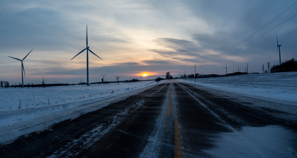 a snow covered road with wind turbines in the distance