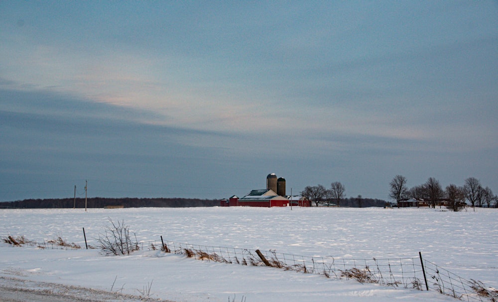 a snow covered field with a barn in the distance