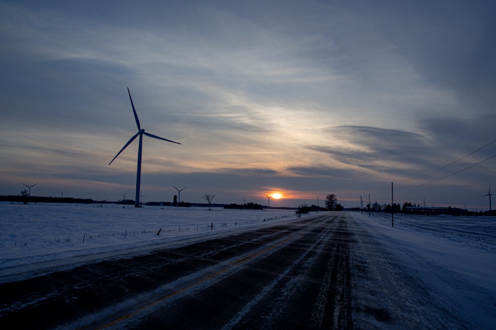a snow covered road with a wind turbine in the distance