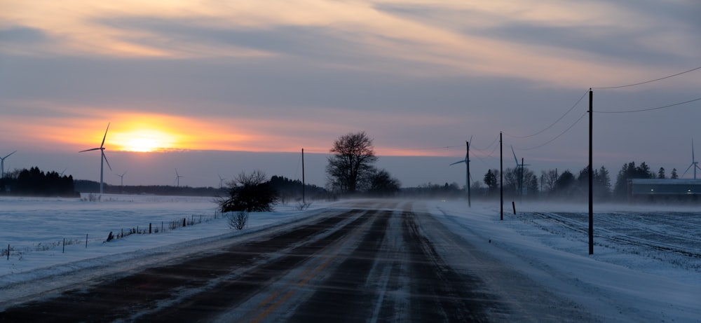 the sun is setting over a snow covered road