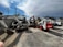 A collection of construction equipment, including multiple Bobcat machines, is parked in an outdoor lot next to a concrete wall. The scene includes excavators and loaders, all lined up on a paved surface under a partly cloudy sky.