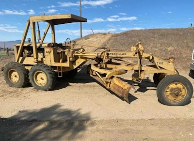Two Caterpillar graders smoothing a dirt road in a desert environment.