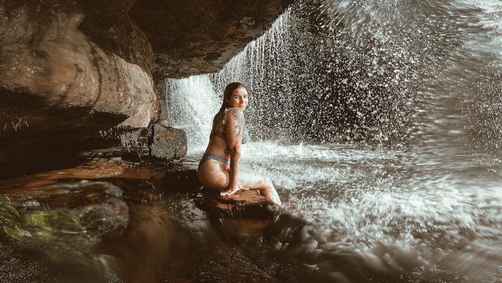 a woman sitting on a rock in the water