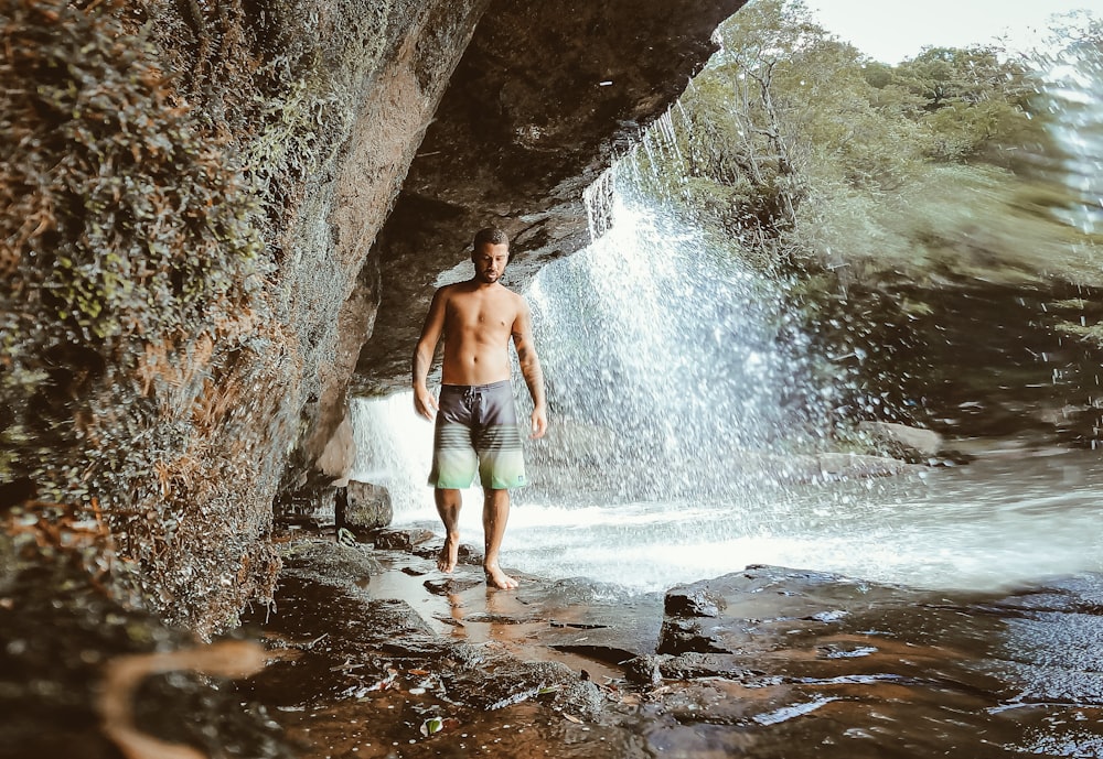 a shirtless man standing in front of a waterfall