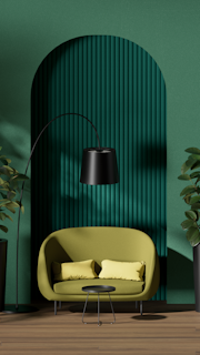 A stylish interior featuring a green circular-patterned wall, a lime green sofa with two matching cushions, a sleek black floor lamp, and a small black coffee table. The space is flanked by tall potted plants, and the wooden floor adds warmth to the modern aesthetic.