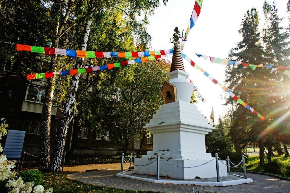 a white monument with a bell in the middle of a park