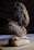 Three loaves of artisanal bread are stacked on top of each other, with intricate designs made from flour on their crusts. They are placed on a wooden surface with a dark, textured background.