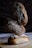 Three loaves of artisanal bread are stacked on top of each other, with intricate designs made from flour on their crusts. They are placed on a wooden surface with a dark, textured background.