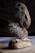 Three loaves of artisanal bread are stacked on top of each other, with intricate designs made from flour on their crusts. They are placed on a wooden surface with a dark, textured background.
