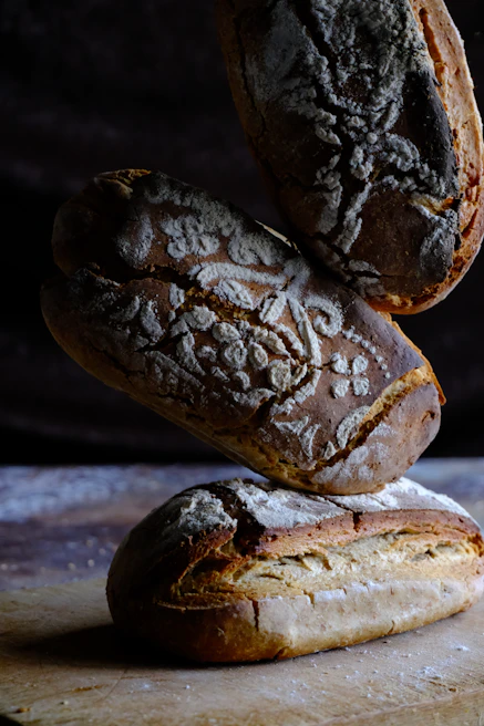 Close-up of artisan breads stacked on a rustic wooden table with natural light highlighting the fresh-milled texture.