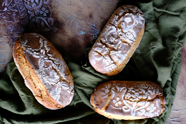 Freshly baked seeded sourdough loaves stacked beside a traditional Armenian patterned cloth.