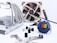 A collection of computer hardware components is arranged on a light surface. There is a large metal CPU cooler with multiple heat pipes on the left side. In the background, a brown and beige computer fan is visible, along with a tube of thermal paste. Several screws, rubber grommets, and mounting brackets are scattered around. Additionally, there is a blue keychain with the 'Core i9' logo prominently displayed.