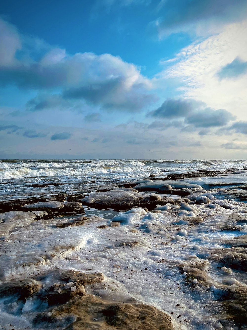 a beach covered in ice and water under a cloudy sky