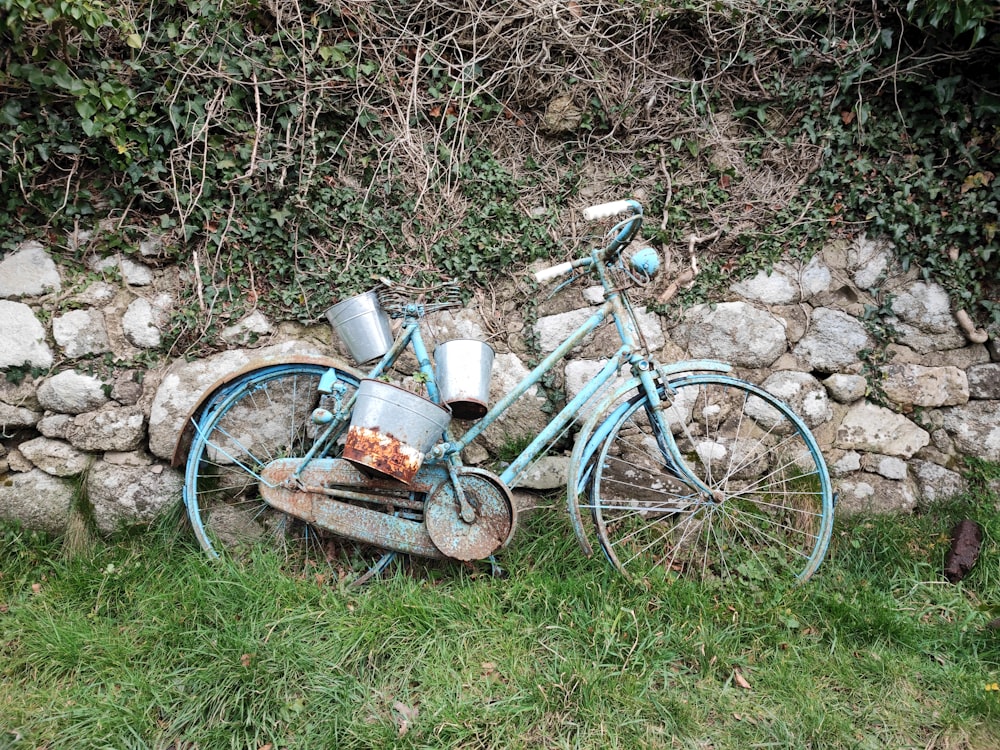 an old rusty blue bicycle leaning against a stone wall