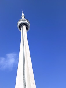 A tall, slender concrete communications tower is seen against a clear blue sky. The tower has a circular observation deck near the top, featuring antennas above it.