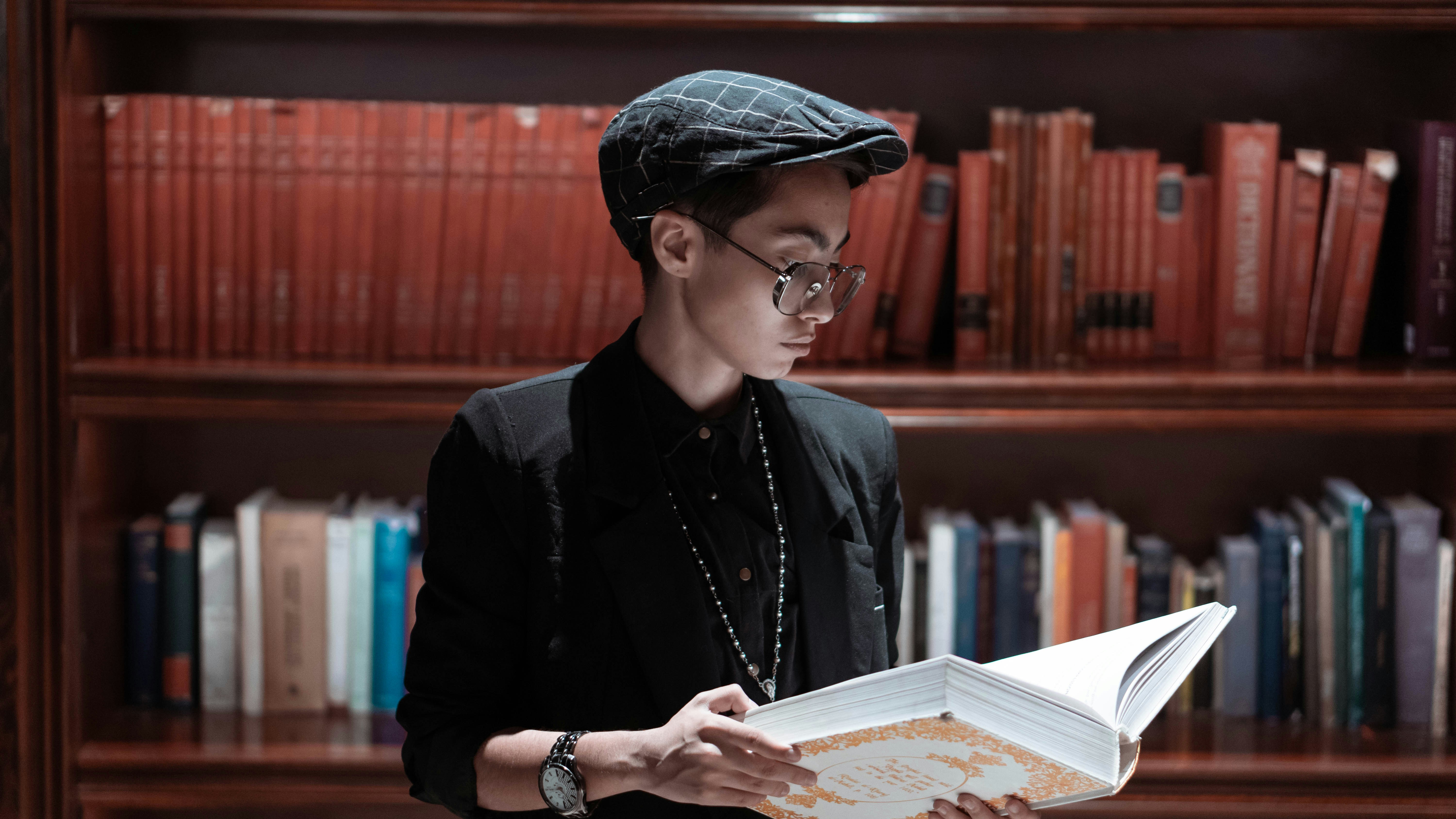 a man reading a book in front of a bookshelf