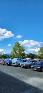 A group of club members standing proudly beside their vintage rust bucket cars under a bright blue sky.