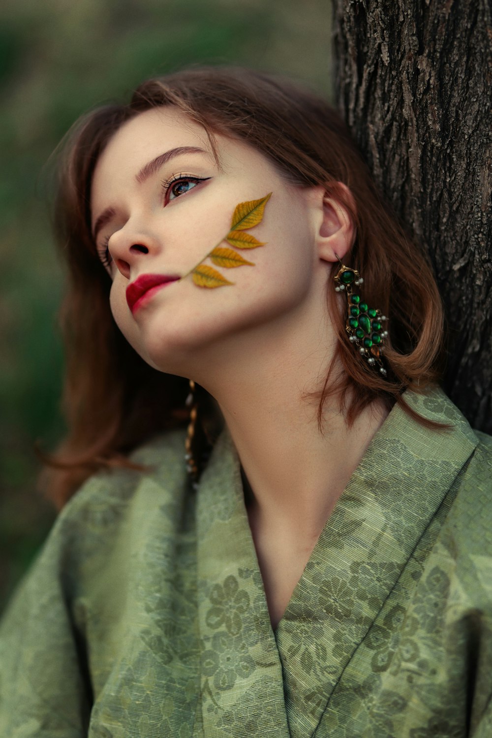 a woman with leaves painted on her face next to a tree