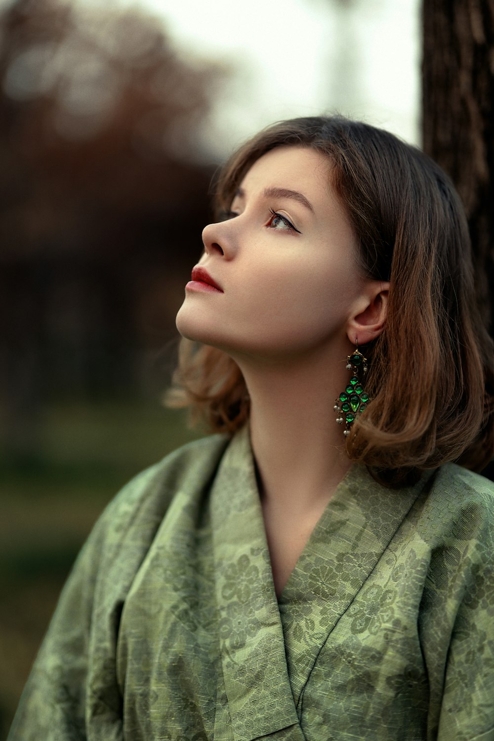 a woman in a green kimono looking up at a tree