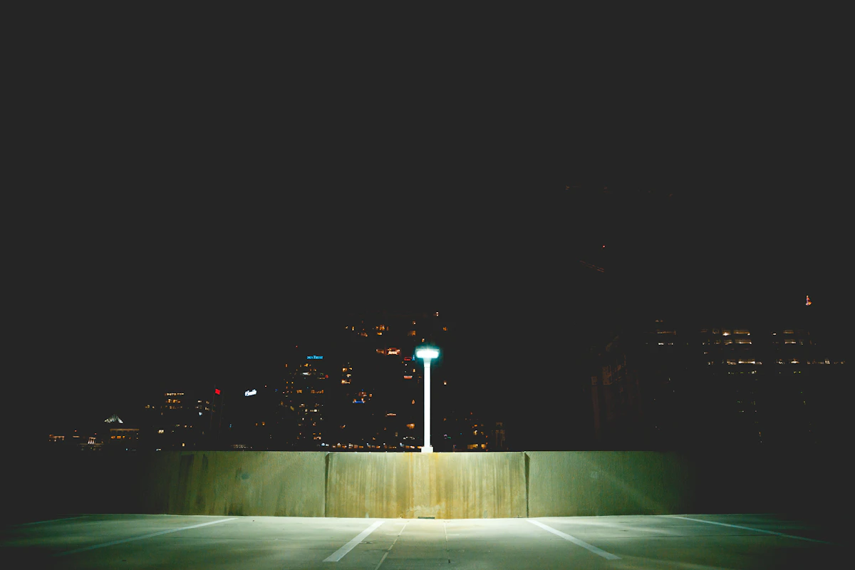 An empty rooftop parking deck at night with a single lamp and distant city lights