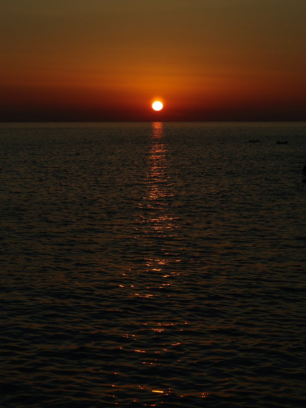 the sun is setting over the ocean with a boat in the water