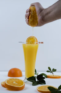 A vibrant glass of freshly poured orange juice with fresh oranges and green leaves around it.