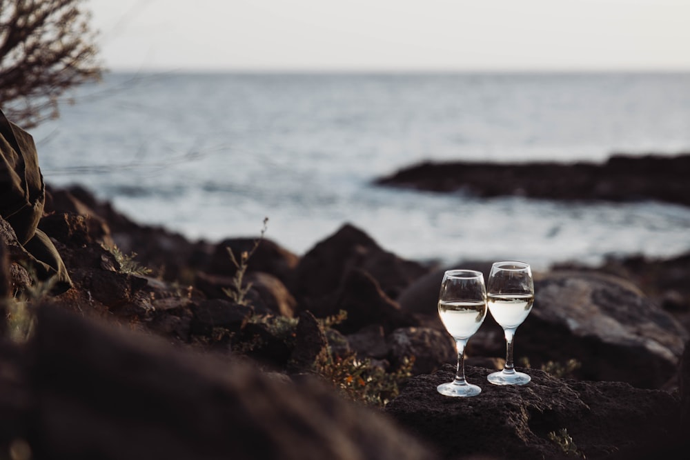 two glasses of wine sitting on a rocky beach
