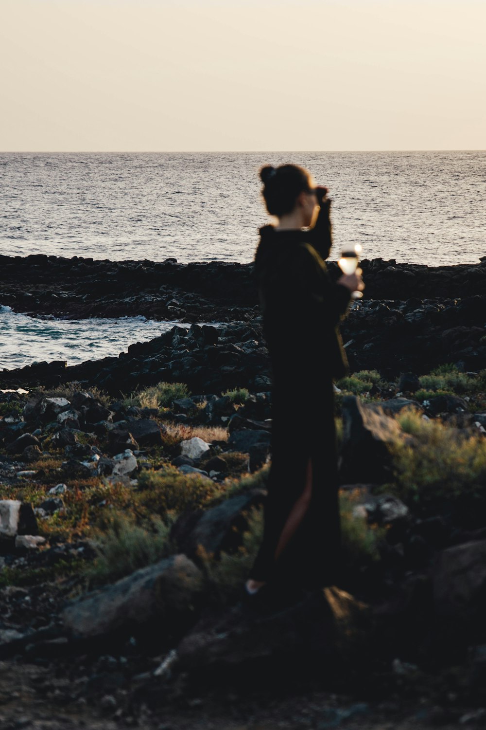 a woman standing on top of a rocky beach next to the ocean