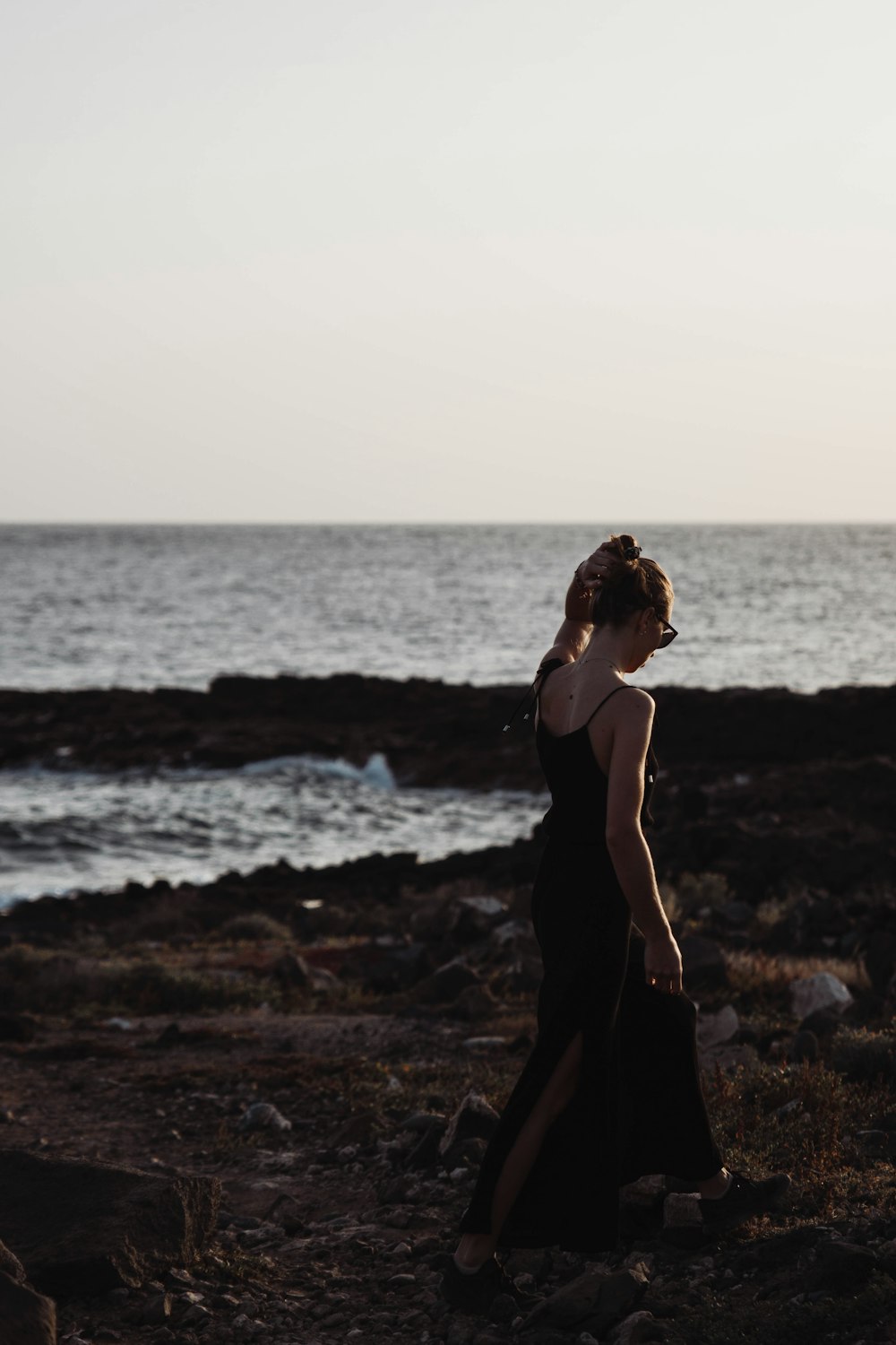 a woman in a black dress walking on the beach