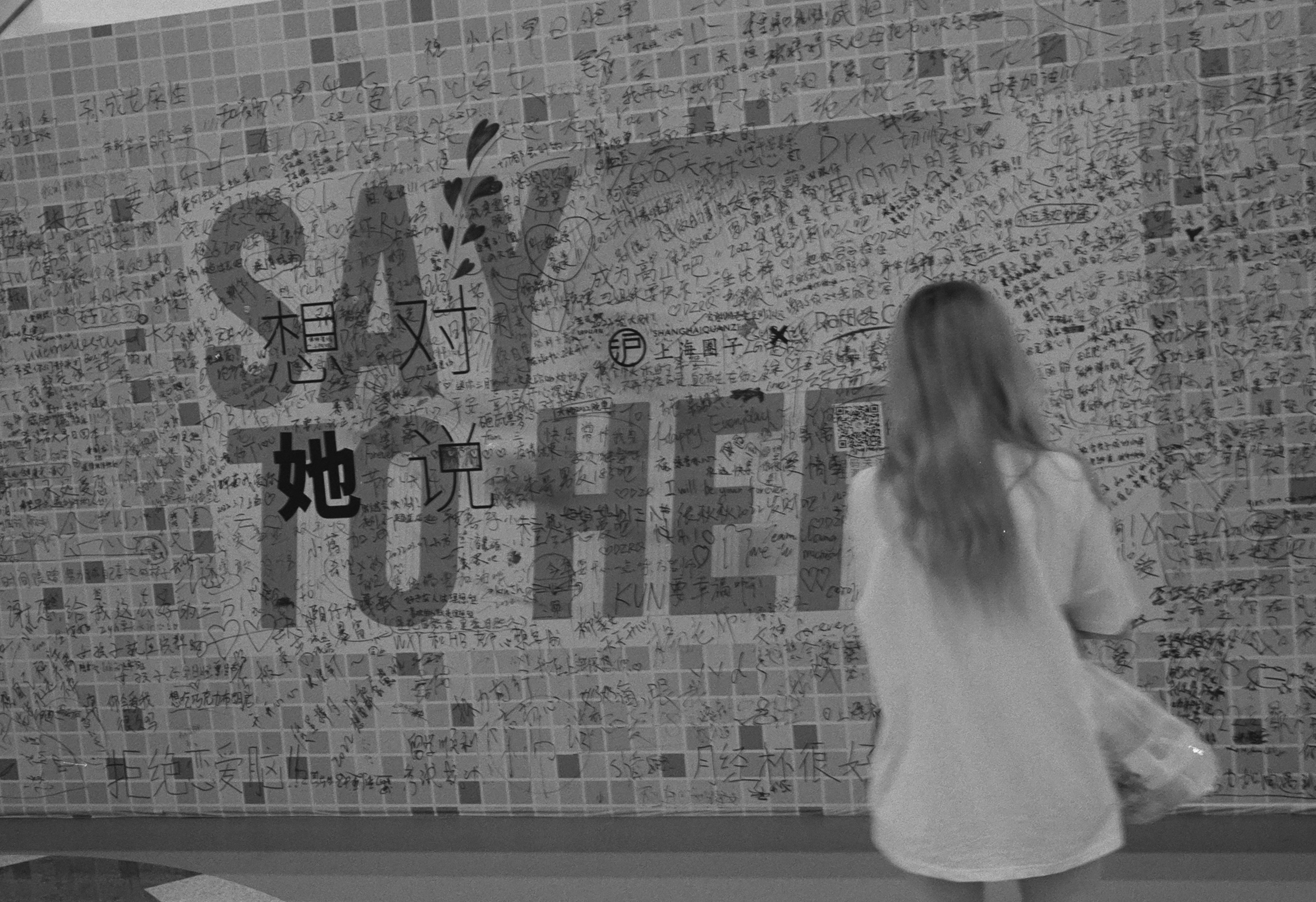 a woman walking past a wall with writing on it