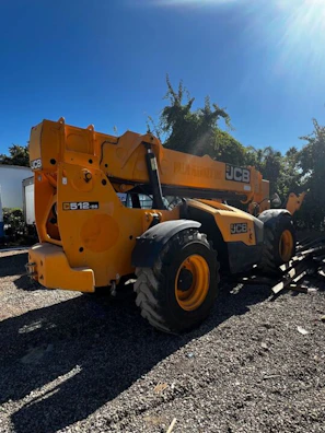 A JCB construction machine parked beside a dirt road with mountains in the distance.