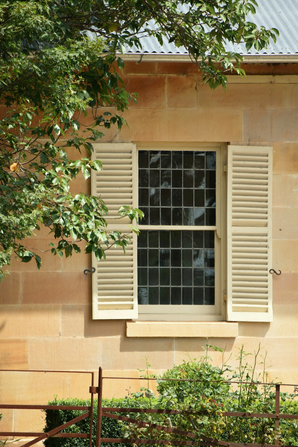 a window with white shutters and a bench in front of it