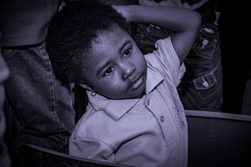 a young boy sitting in a chair with his hands on his head