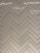 A herringbone pattern made of rectangular tiles with a glossy finish. The tiles are arranged in a diagonal zigzag layout, creating an intricate and visually appealing design. The surface reflects light, adding a sleek and modern feel.