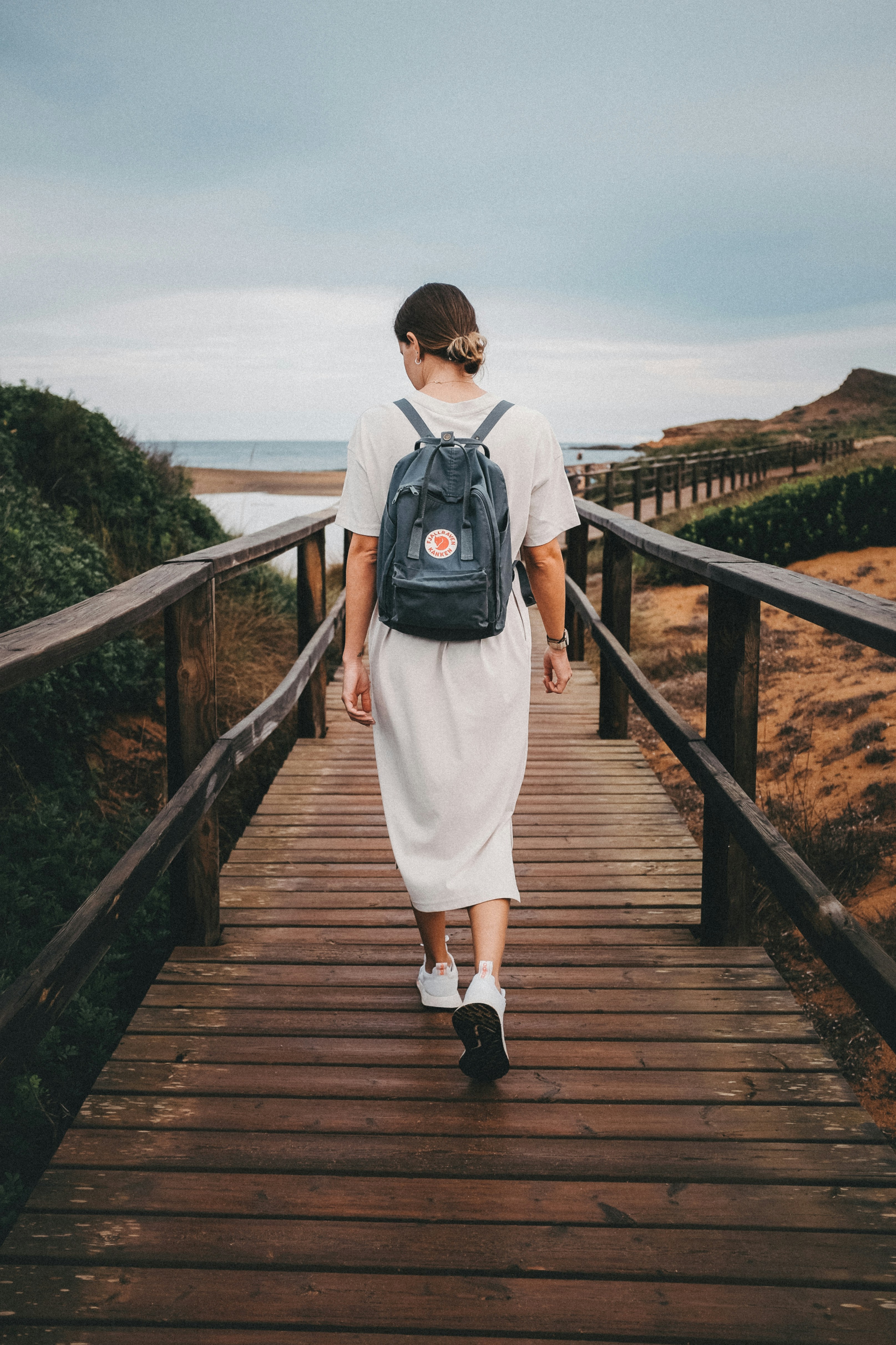 a woman walking across a wooden bridge with a backpack on her back