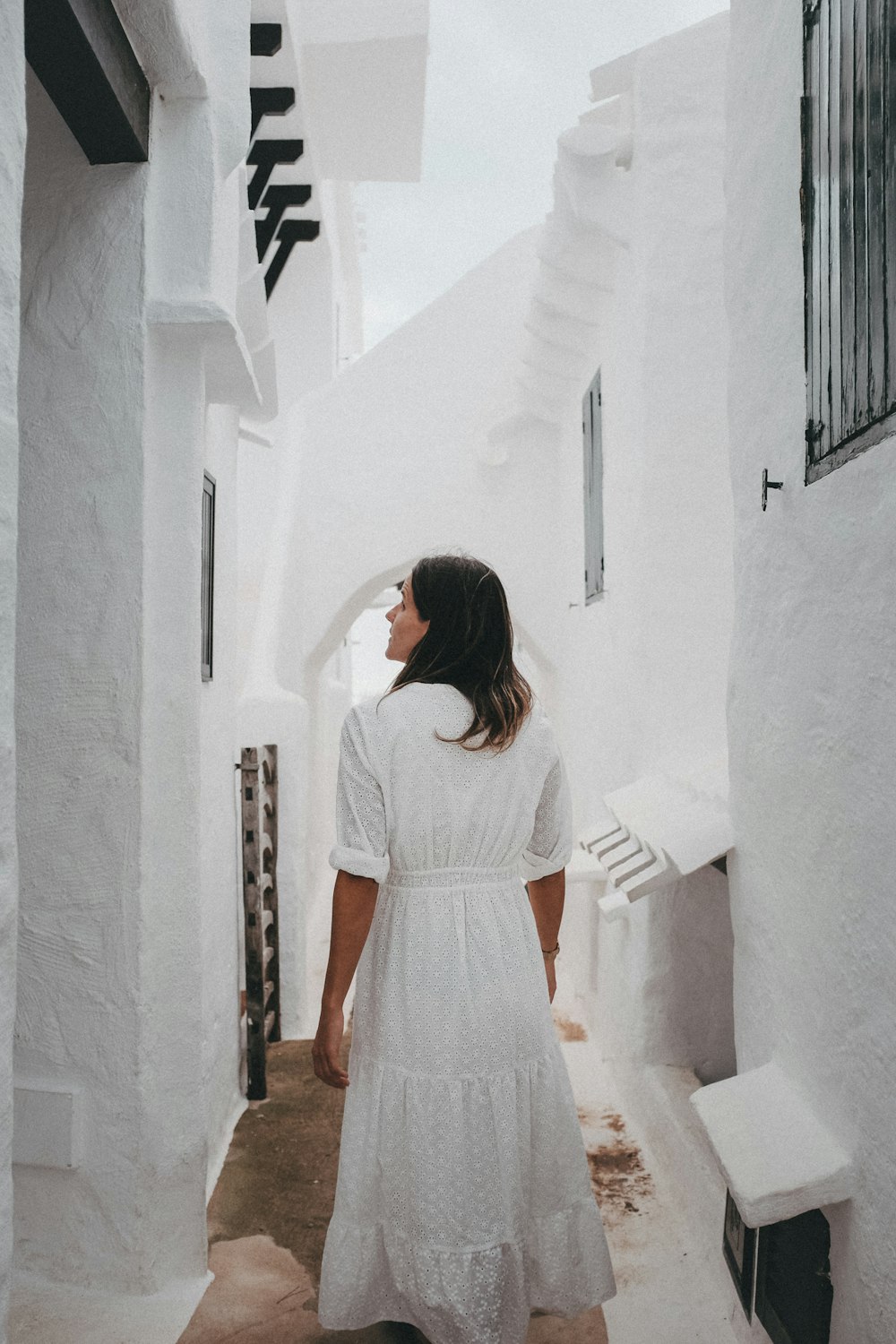 a woman in a white dress walking down a narrow alley way