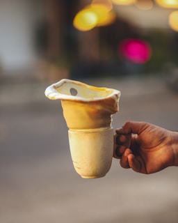 A hand is holding a uniquely designed ceramic cup, which appears to have a melted or distorted top portion, forming an abstract shape.