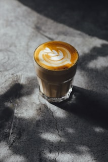 Iced latte with swirling cream in a clear glass, resting on a matte black table with soft natural light.