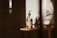 A glass bottle with a pump dispenser is placed on a wooden surface, illuminated by warm, natural light casting long shadows. The label on the bottle suggests it contains shea butter oil. The overall setting is minimalist, with a soft, earthy aesthetic.