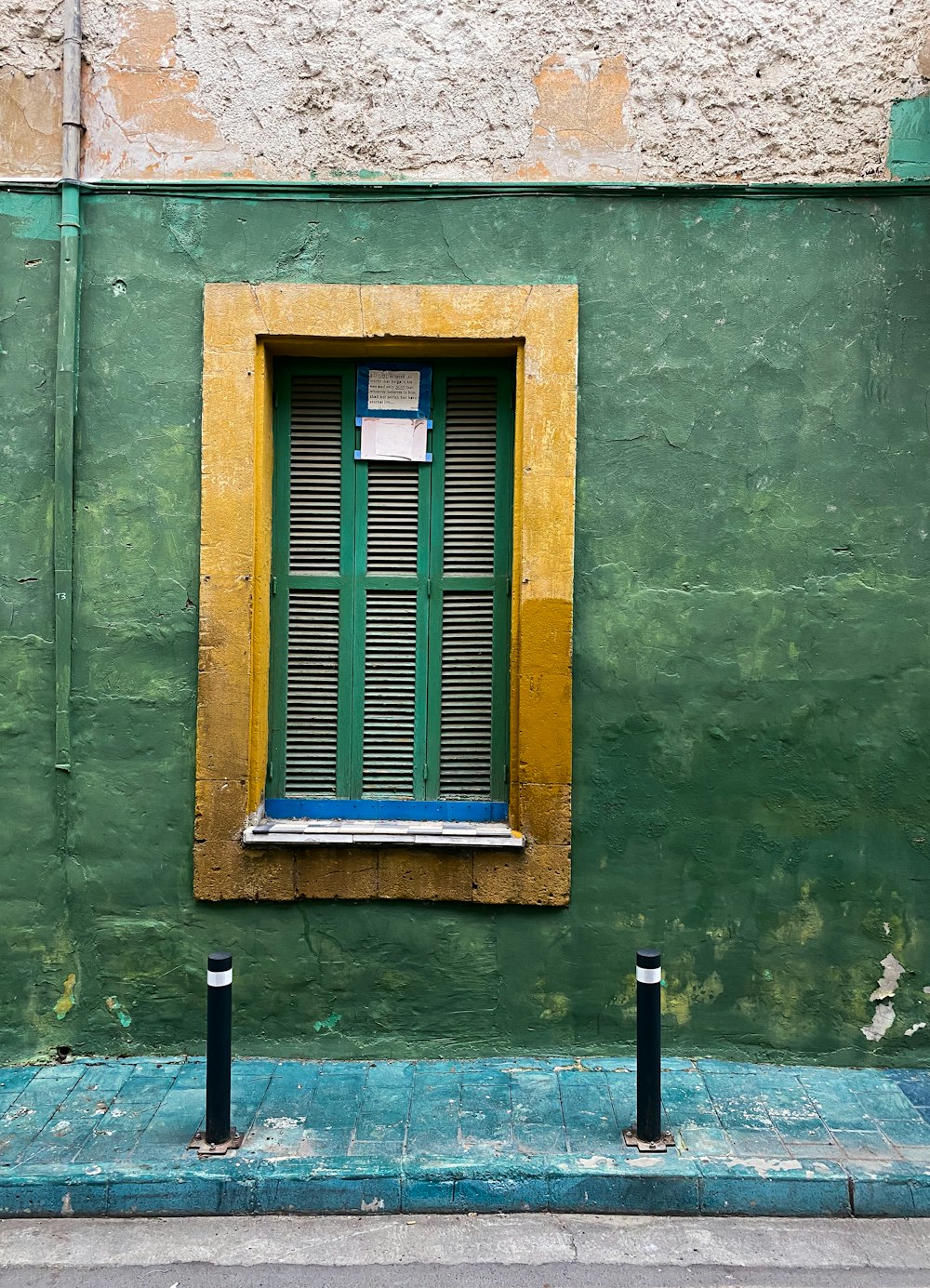 a green wall with a yellow window and two black poles