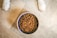 A bowl filled with brown dog kibble sits on a tiled floor, with two white paws visible on either side.
