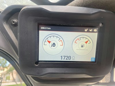 A digital screen displaying vehicle dashboard indicators. It shows two circular gauges; the left one depicts an engine temperature gauge with a water symbol, and the right one indicates a fuel gauge. The top left corner displays the hours used, reading 298.5 hrs, and the bottom shows a digital number 1720 with a lighting symbol beside it. The screen is surrounded by a black frame held in place by a bolt.