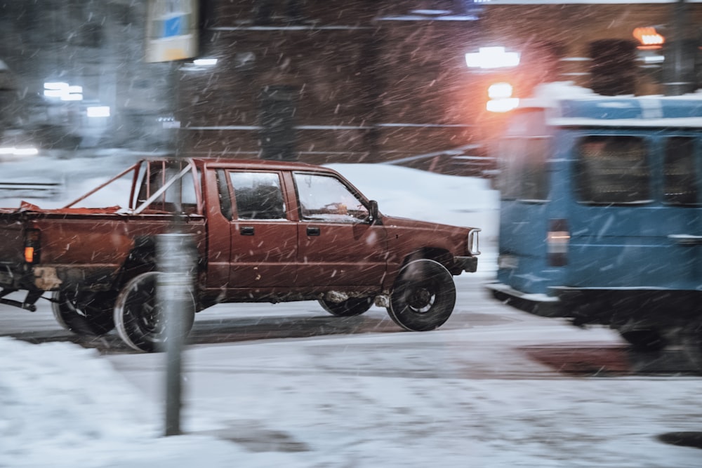 a red truck driving down a snow covered street