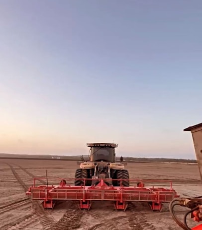 A tractor equipped with heavy-duty tires parked in a vast green field at dawn.