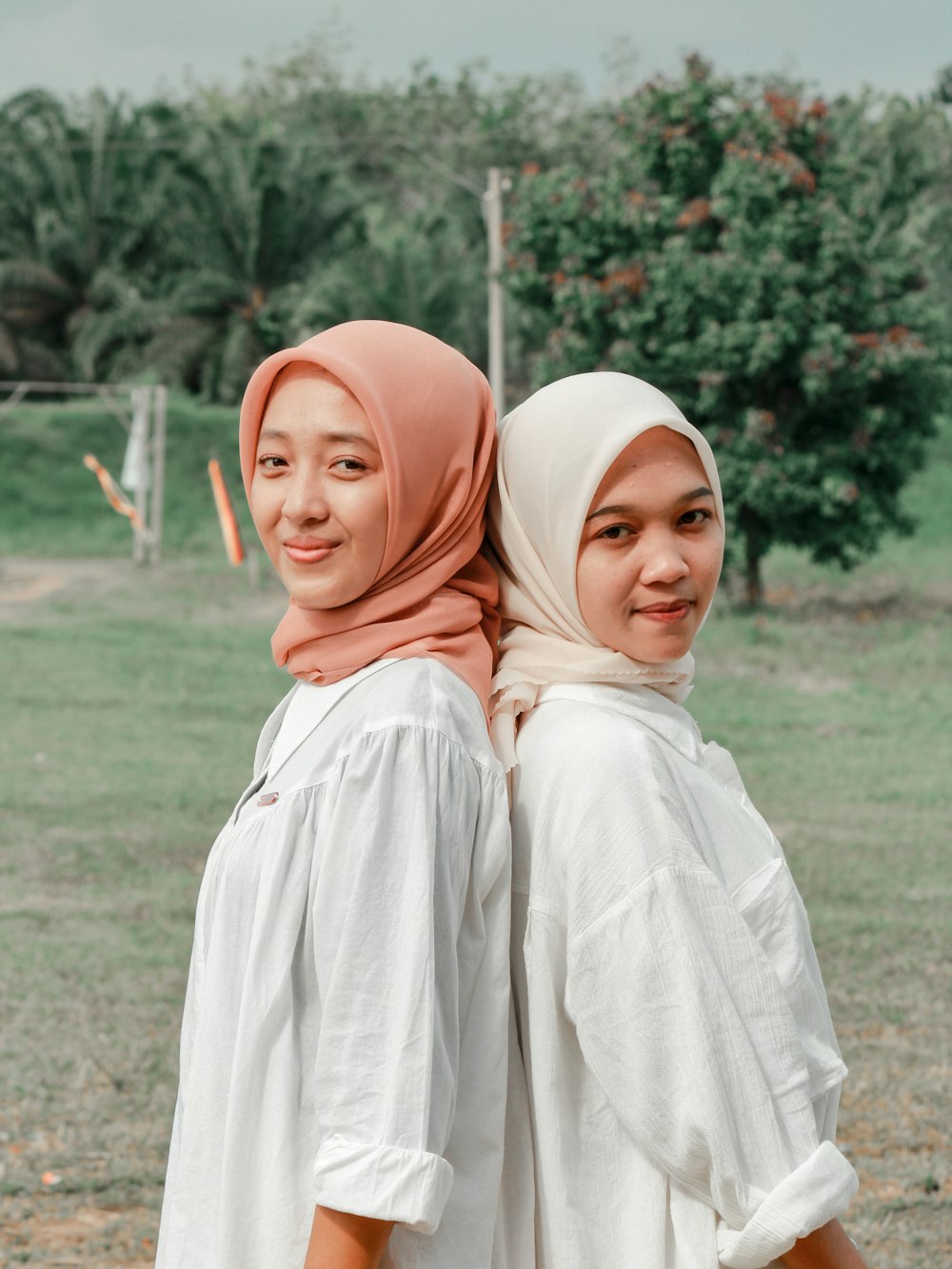 two women wearing headscarves standing in a field