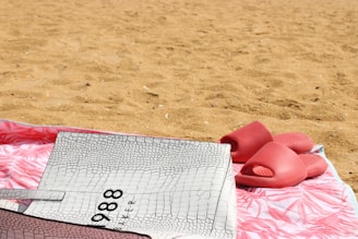 A pair of stylish sandals and waterproof phone pouches arranged neatly on a sandy beach towel