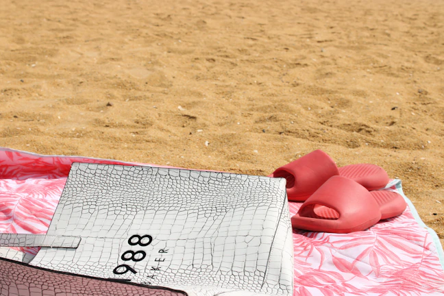 A close-up of a Louis Vuitton bag resting on soft sand with gentle waves in the background.