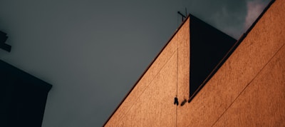 A geometric composition featuring part of a building with a warm, textured facade against a moody, dark sky. The contrast between the angular lines and the shadows creates a dramatic effect.