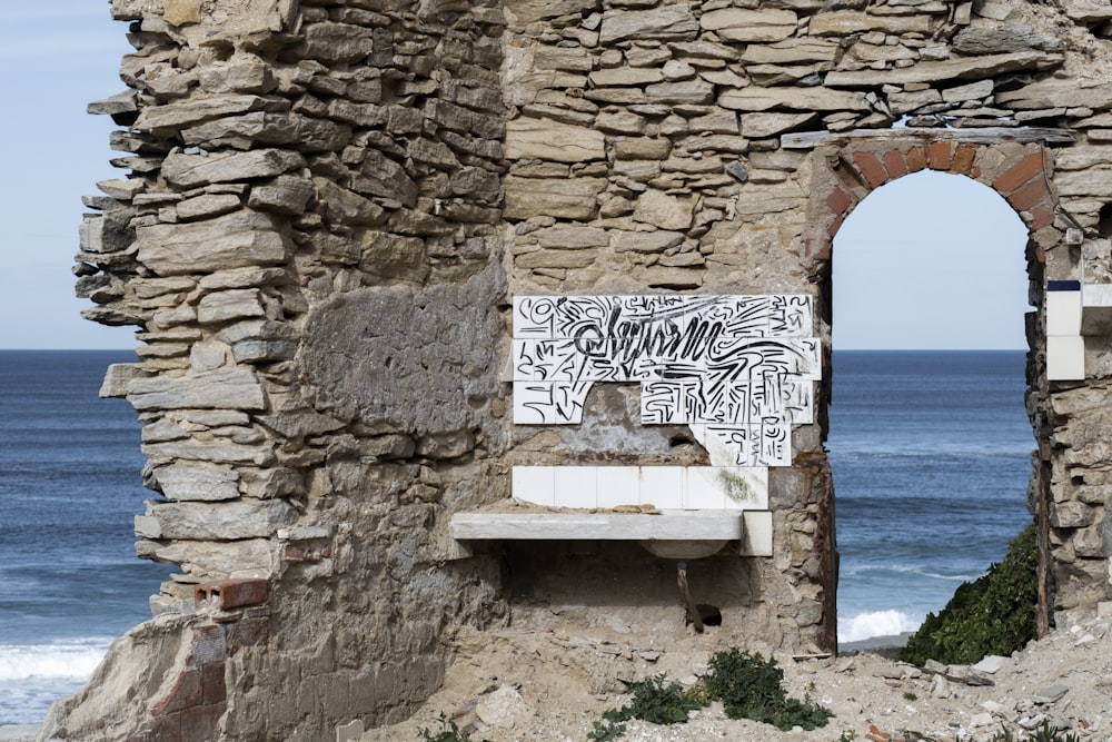 a stone wall with graffiti on it next to the ocean