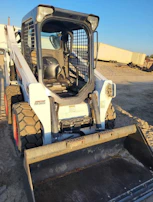 Skid steer spreading gravel evenly across a driveway surface.